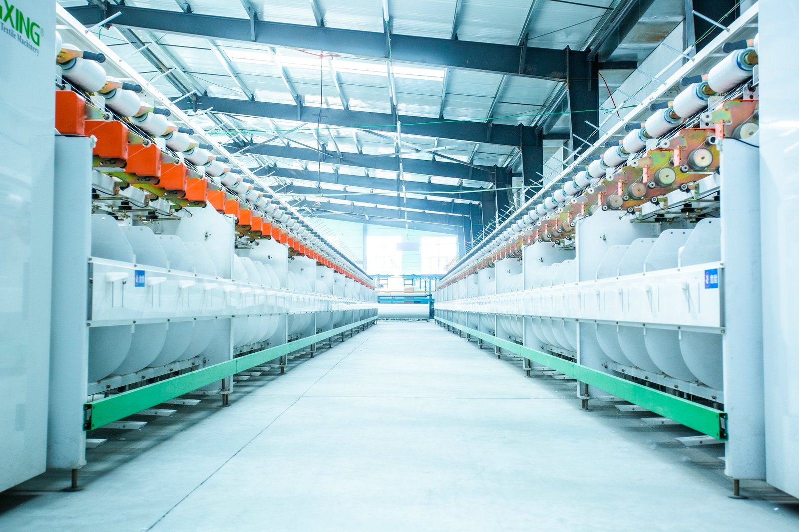 A wide perspective view of a modern production facility for concrete mattresses, featuring large weaving machines lined up with bright lighting overhead. The machines display spools of fabric material, indicative of the advanced technology used in crafting durable, environmentally friendly concrete mattresses. The clean, industrial workspace reflects a commitment to quality manufacturing in the concrete mattress industry.