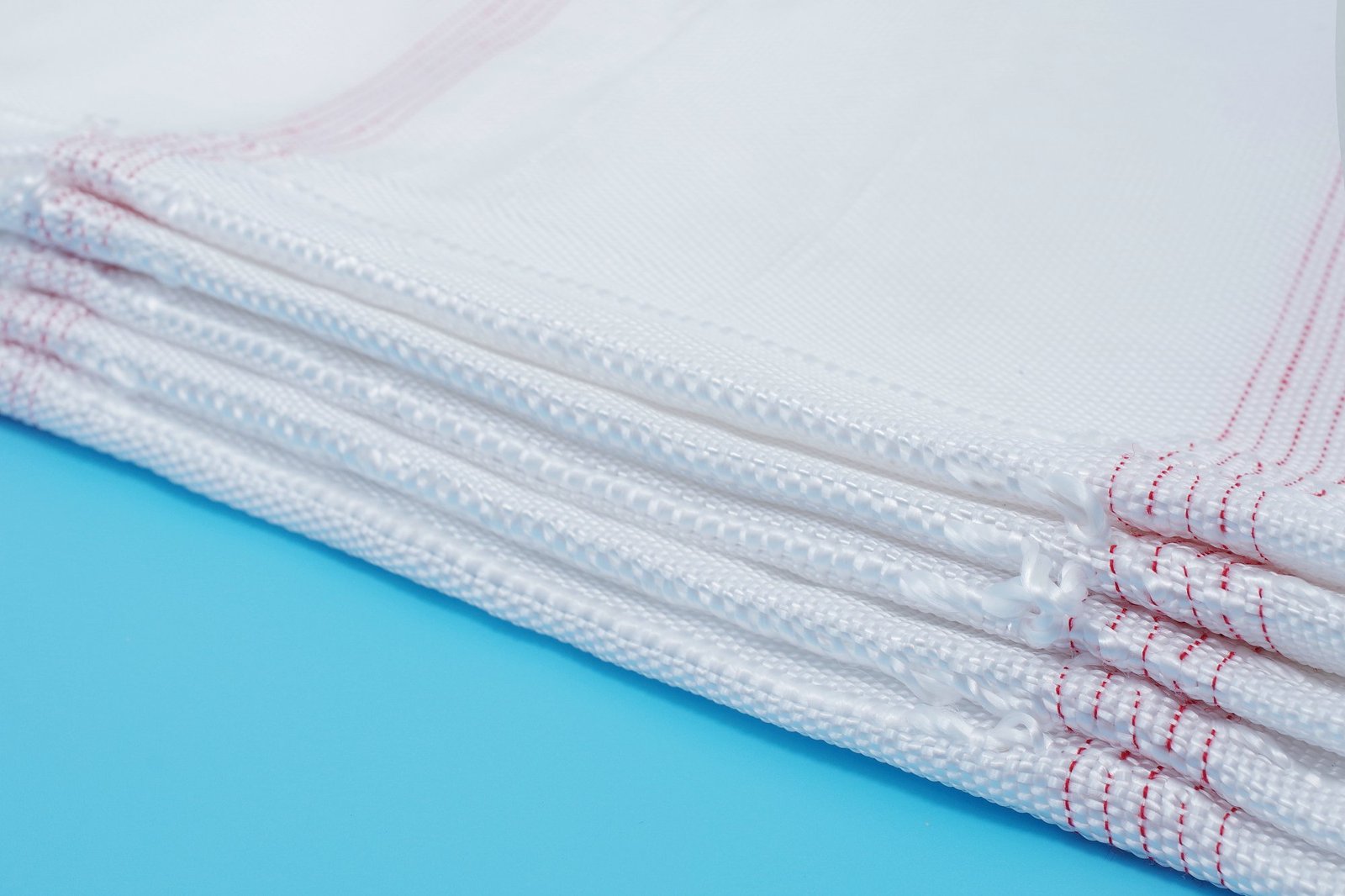 Close-up of folded articulated concrete mattress bags displaying a woven texture, with red stitching on the edges, set against a blue background. The synthetic material is designed for durability in civil engineering applications, representing a critical component in erosion control projects.