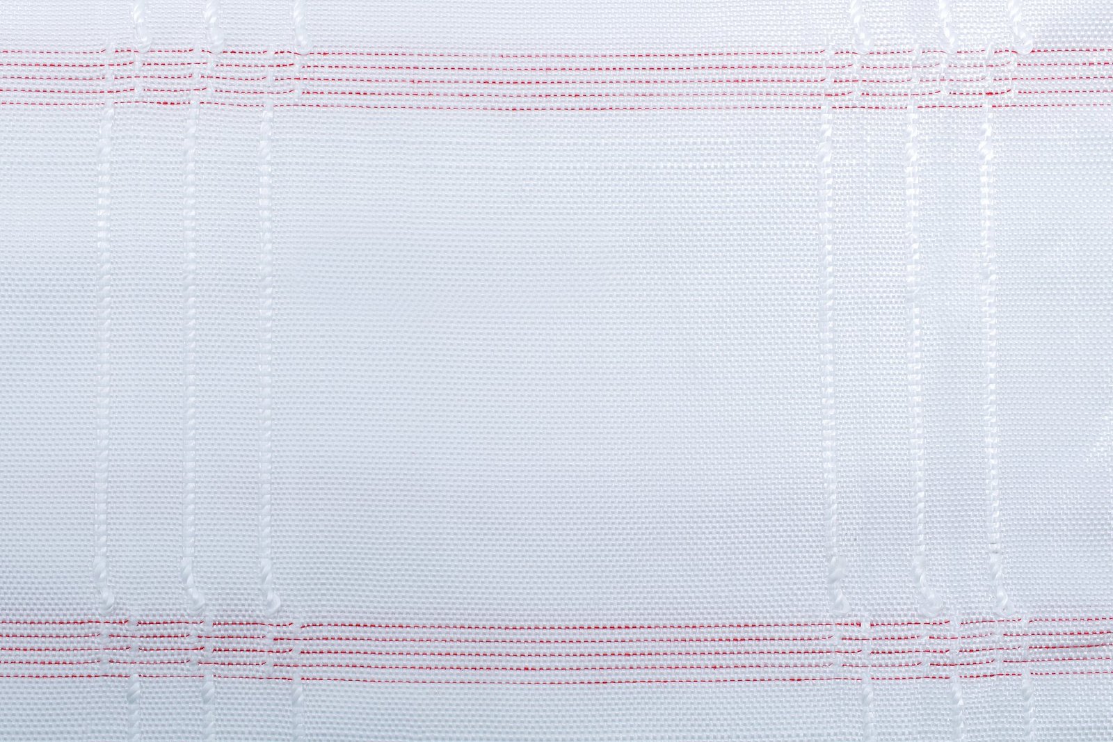 Close-up view of woven polypropylene fabric, showcasing a textured surface in white with red stitching. This fabric is commonly used in the production of articulated concrete mattresses, designed for strength and durability in engineering applications.
