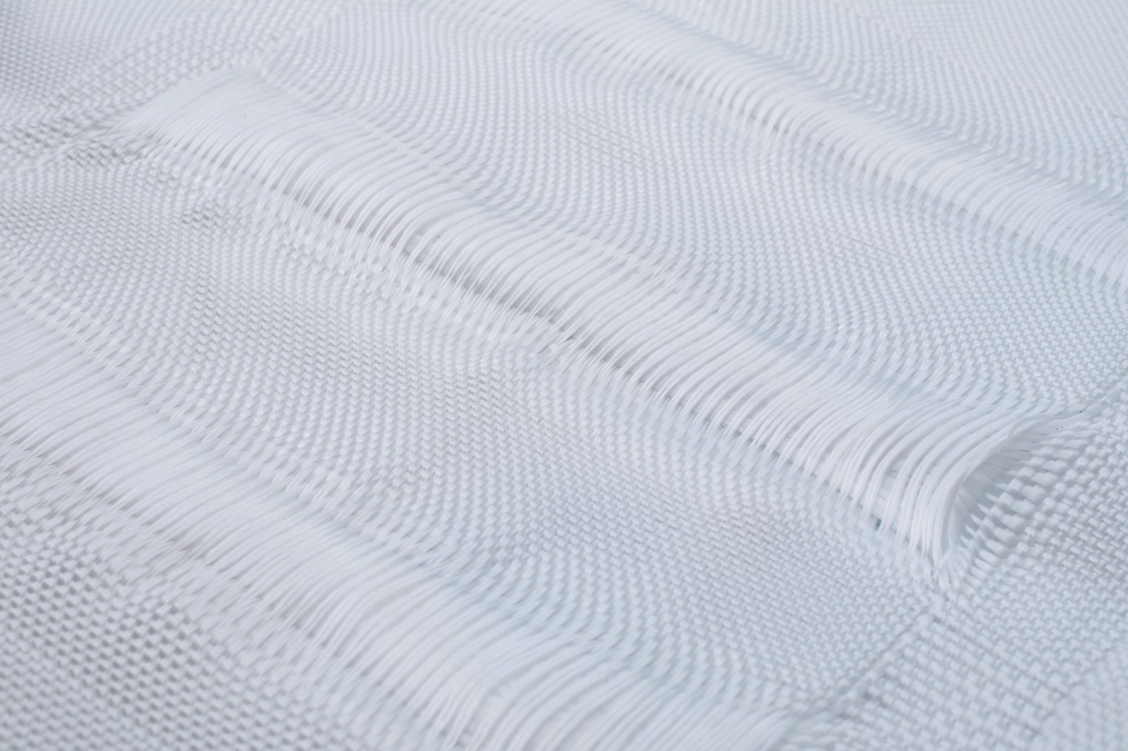 Close-up of a textured concrete mattress made from synthetic fibers, showcasing the intricate woven pattern and layered structure. The white, non-woven fabric appears smooth, highlighting its durability and permeability, ideal for erosion control applications in civil engineering projects.