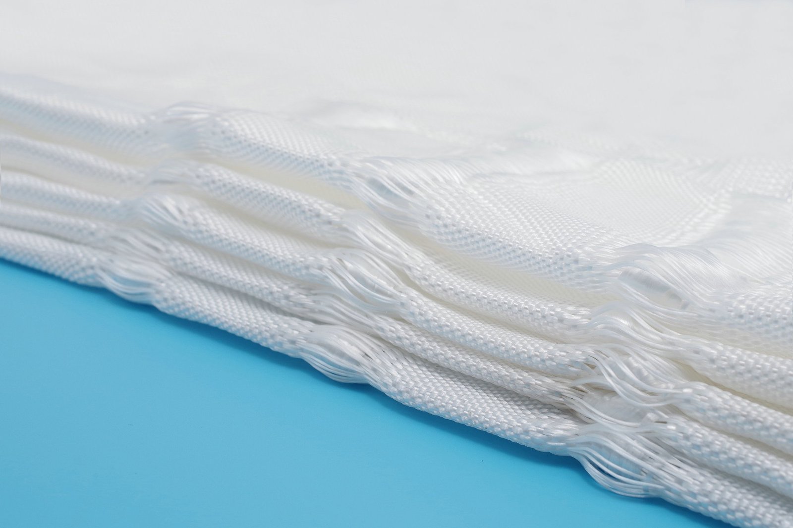 Close-up of a white woven fabric designed for articulated concrete mattress production, showcasing its layered structure and textured appearance. The synthetic fibers are neatly arranged, highlighting the fabric's strength and durability, making it suitable for various civil engineering applications. This image emphasizes the essential components used in creating permeable and effective concrete mattresses.