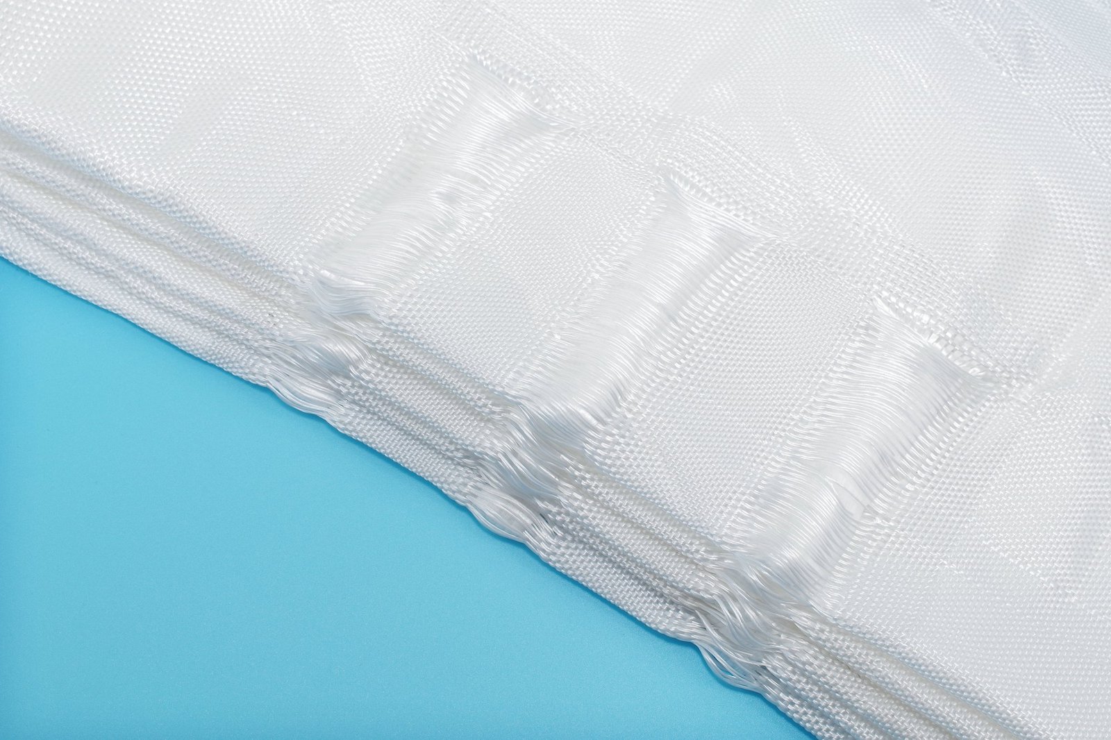 Close-up view of articulated concrete mattress material, featuring a textured weave made from synthetic fibers, showing multiple layers stacked on a blue surface, demonstrating both flexibility and strength. This image highlights the durable fabric's ability to contain and protect against erosion in civil engineering applications.