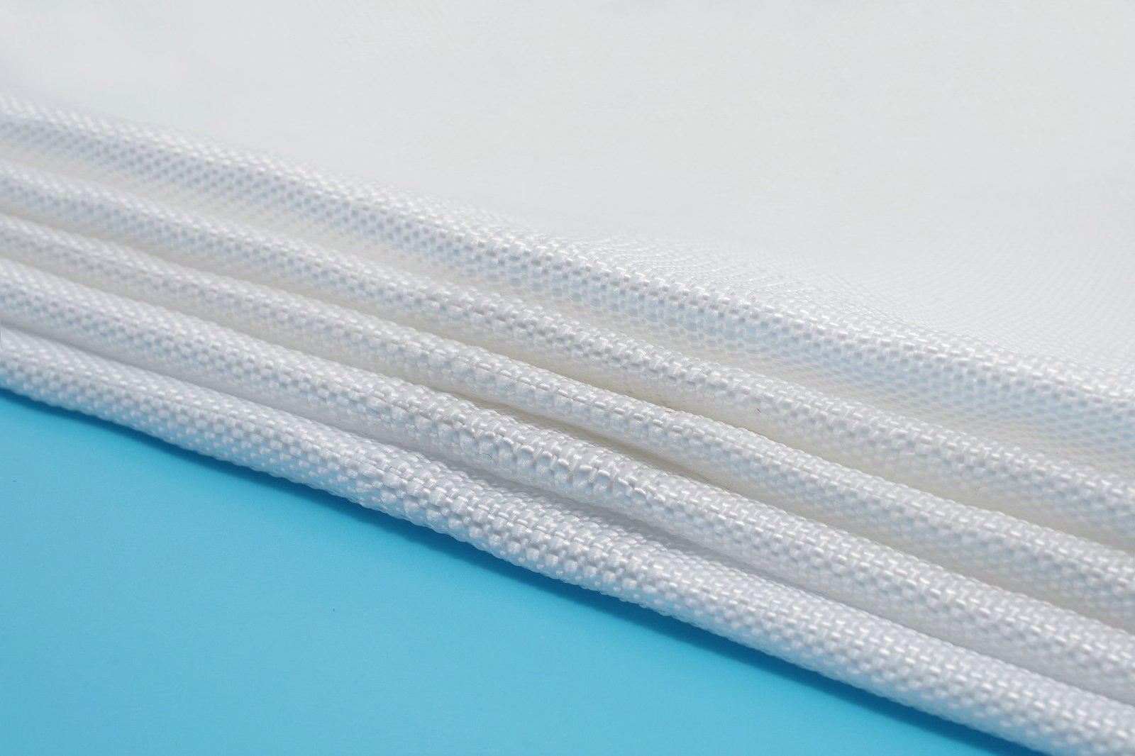 Close-up view of folded articulating concrete mattress material, showcasing its woven synthetic texture with a white finish. The fabric is layered flat, highlighting the structural integrity and flexibility suitable for various civil engineering applications. The image emphasizes the material's permeable properties and resilience, essential for erosion control and stability in construction projects.