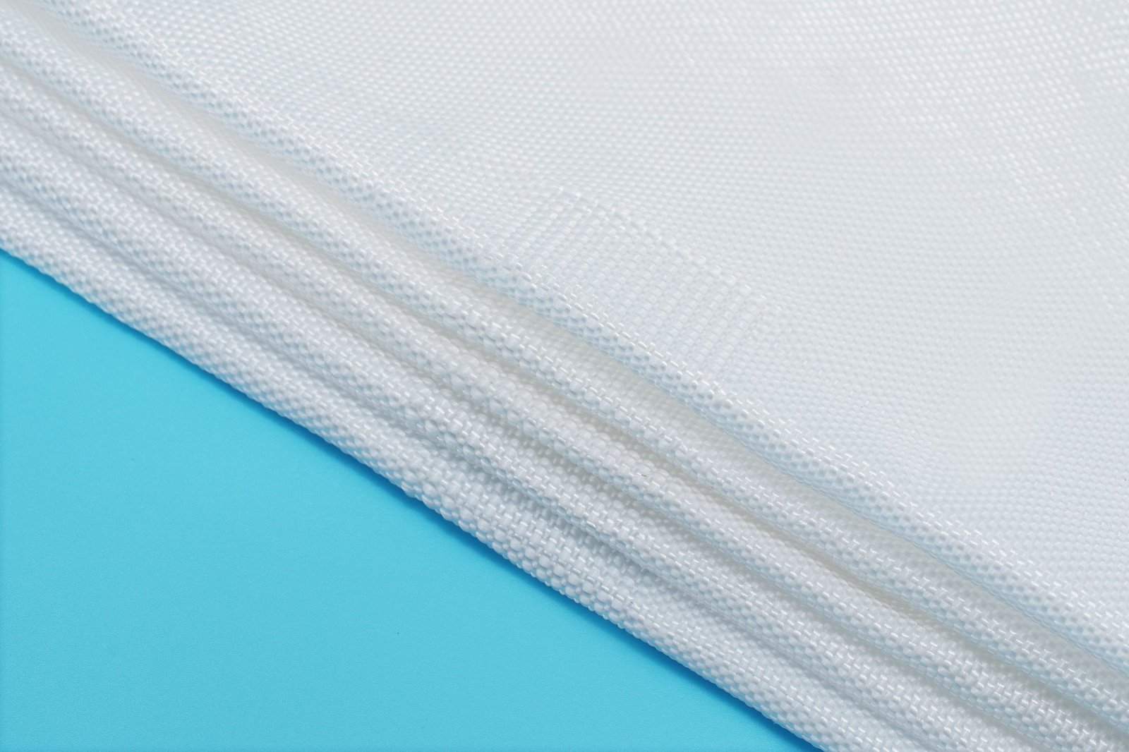 Close-up of layered synthetic fabric resembling articulated concrete mattress material, showcasing a woven texture against a soft blue background. The fabric is designed for water filtration and erosion control, emphasizing durability and permeability. Ideal for civil engineering applications.